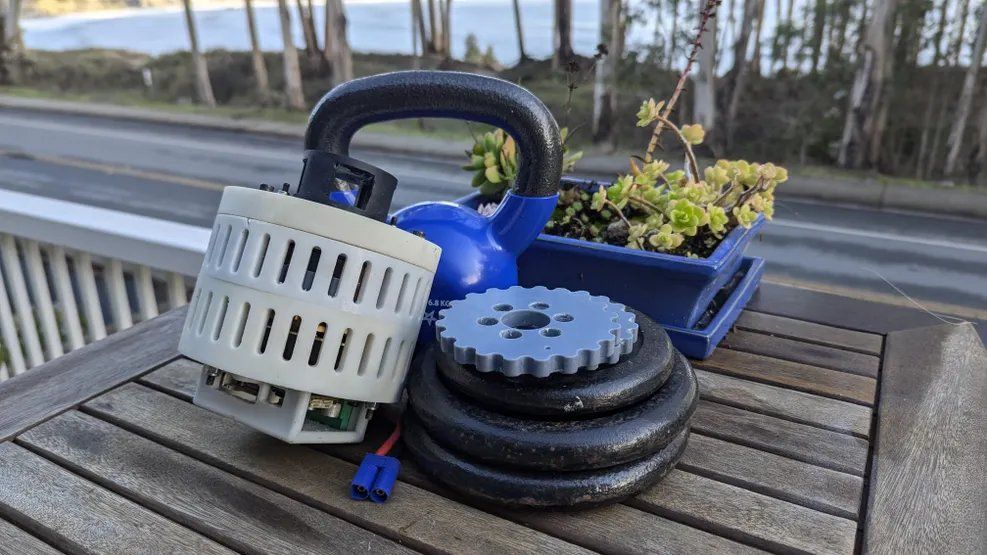 OpenCycloid actuator lifting a kettlebell on a lever during a load test, with spare cycloidal disks on stacked weight plates.