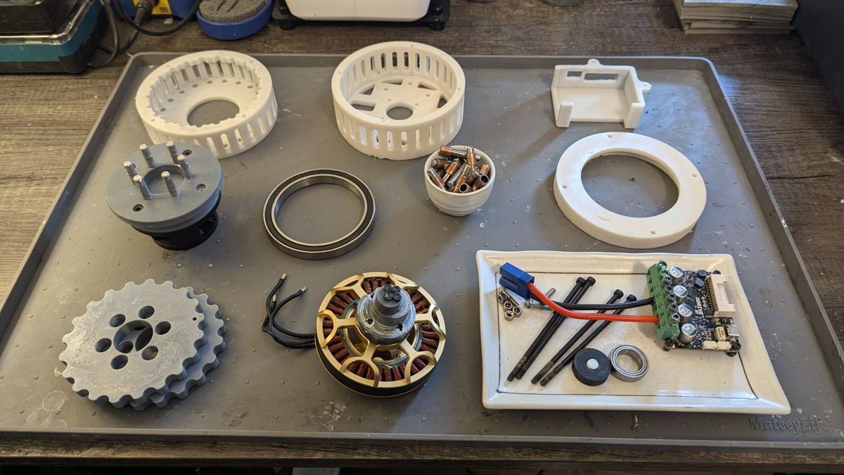 OpenCycloid components laid out on a tray: printed housings and disks, ring pins, output bearing, brushless motor and drive.